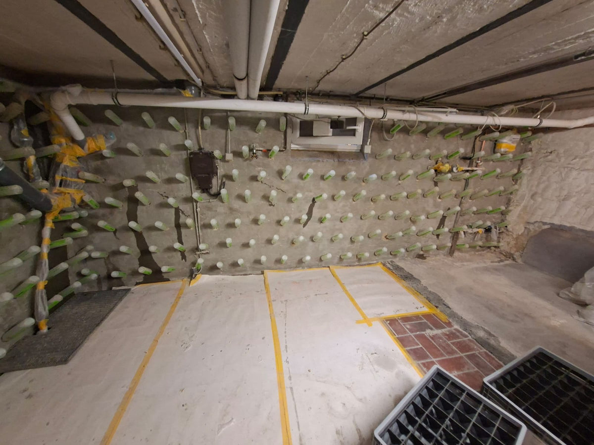 Kellerwand mit dichtem Raster aus Injektionspackern, daneben die abgeklebte Bodenabdeckung der Baustelle