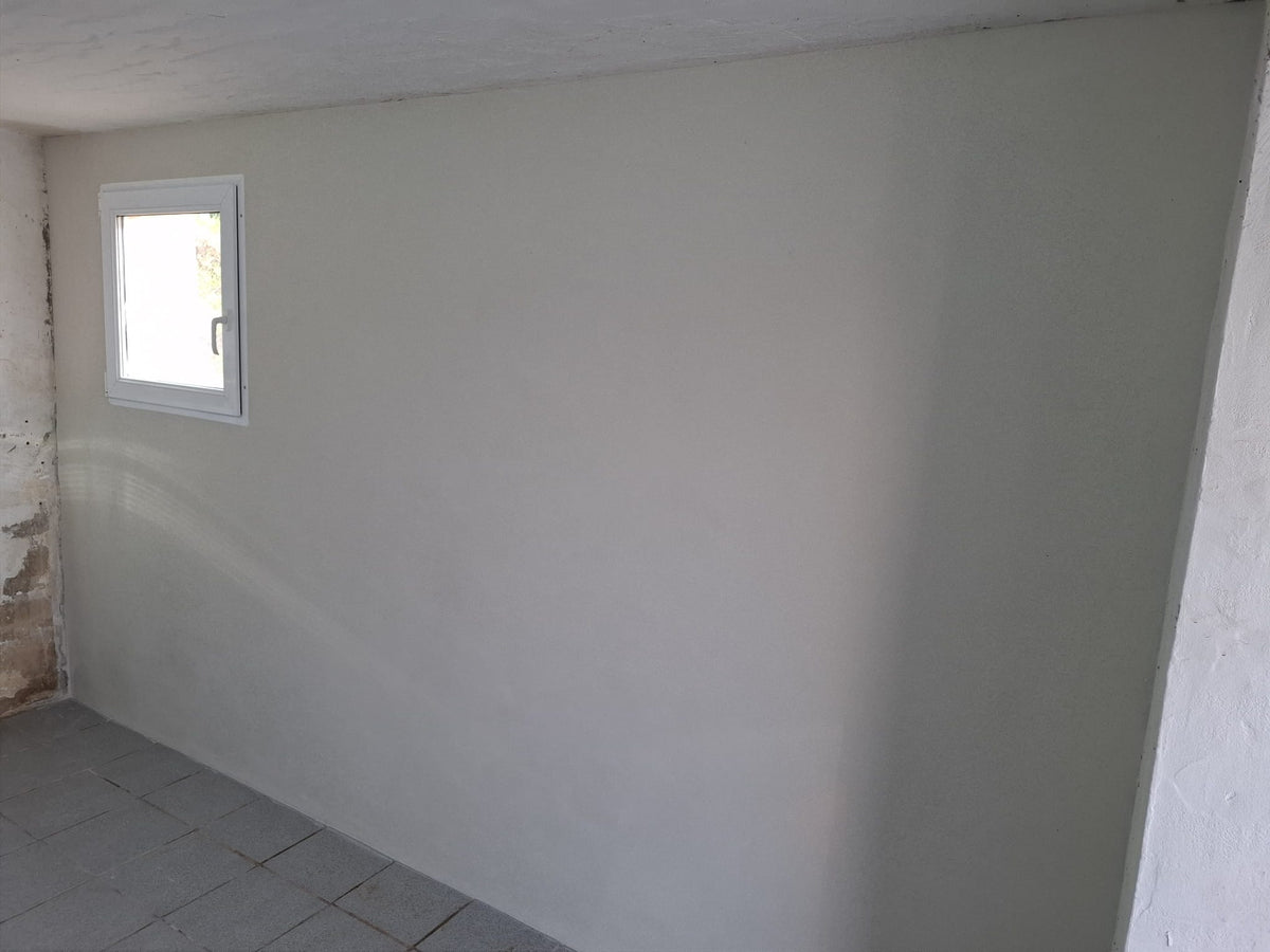 Fertig verputzte, glatte Kellerwand mit Fenster nach der Sanierung