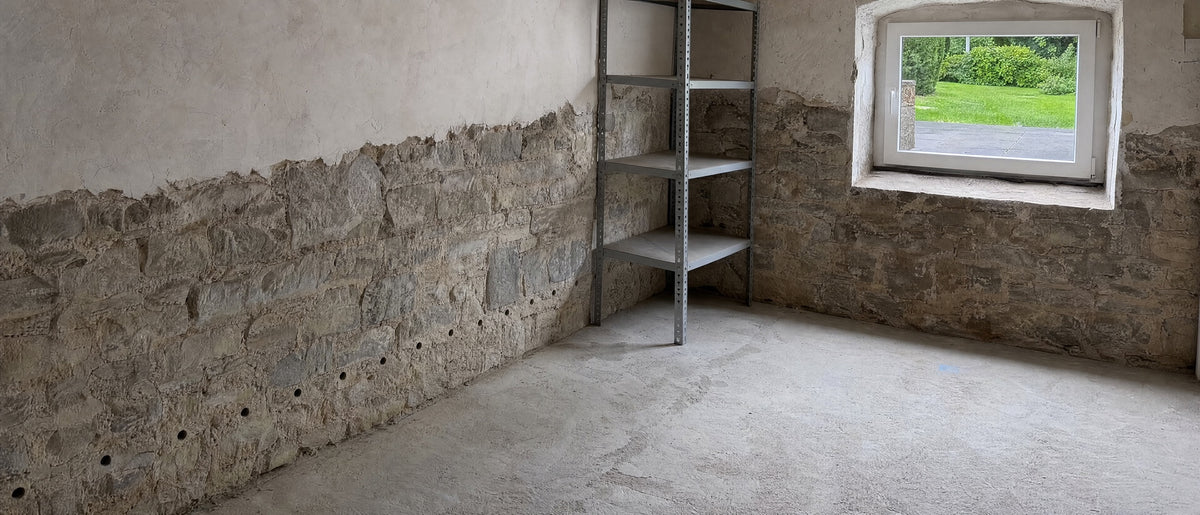 Kellerwand mit einer Reihe Bohrlöcher über dem Boden, draußen vor dem Fenster unberührter Garten